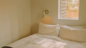 Un dormitorio con cama, almohadas, una lámpara de pared y una ventana con vistas.