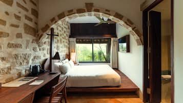 Un dormitorio con pared de piedra, cama, escritorio y ventana con cortinas.