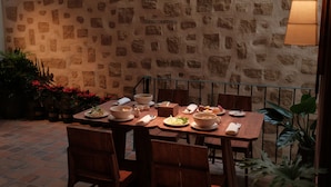 Un espace extérieur aménagé pour les repas, avec des murs en pierre, une table dressée pour deux personnes et entouré de chaises.