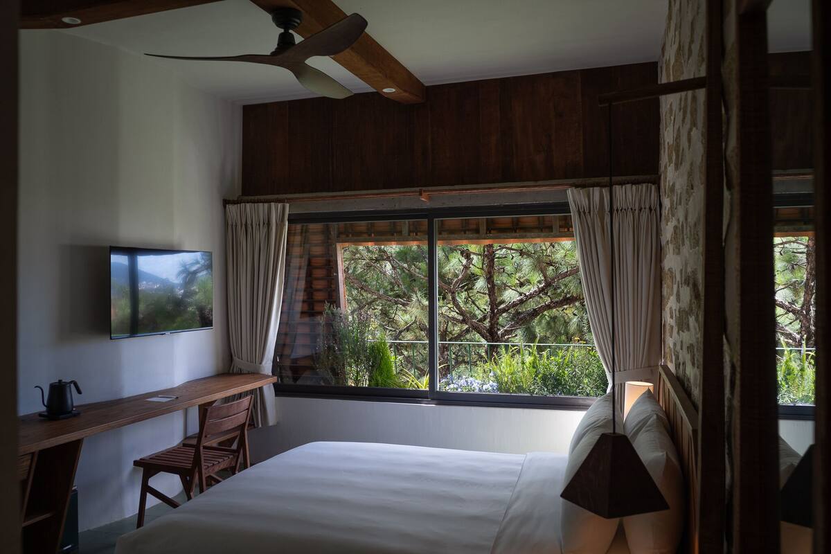 A bedroom with a large window, wooden ceiling, and a bed with white linens.