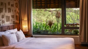 Un dormitorio con un ventanal grande, una pared de piedra y una cama con ropa de cama blanca.