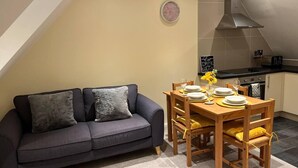 A cozy living area with a dark grey sofa, a wooden dining table set with plates and glasses, and a kitchen in the background. - Central location 2-Bed Apartment in Maidstone (Maidstone)