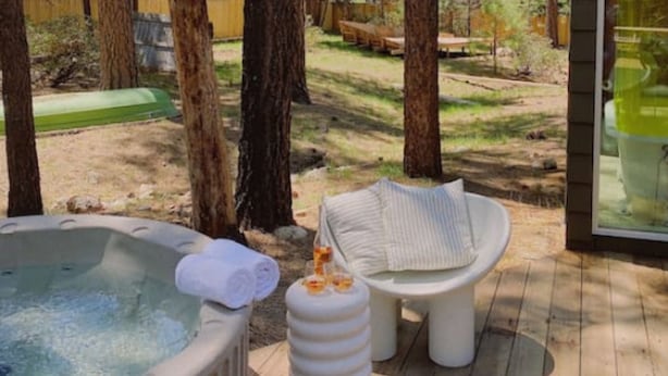 A hot tub, a small table with a cushion, and a glass enclosure in a wooded outdoor area. - Colorado Lodge Big Bear California / C4 (Big Bear Lake)