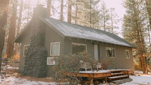 A cabin with a stone chimney, a porch with benches, and a view of the surrounding forest. - Colorado Lodge Big Bear California / C4 (Big Bear Lake)