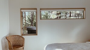 A room with a bed, a wicker chair, and two windows with forest views. - Colorado Lodge Big Bear California / C4 (Big Bear Lake)