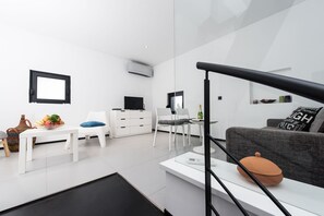 A modern, minimalist living space with a white sofa, a dining table, and a kitchen area.