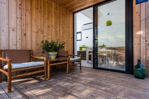 A wooden deck with two wicker chairs and a table, a potted plant, and a green vase.