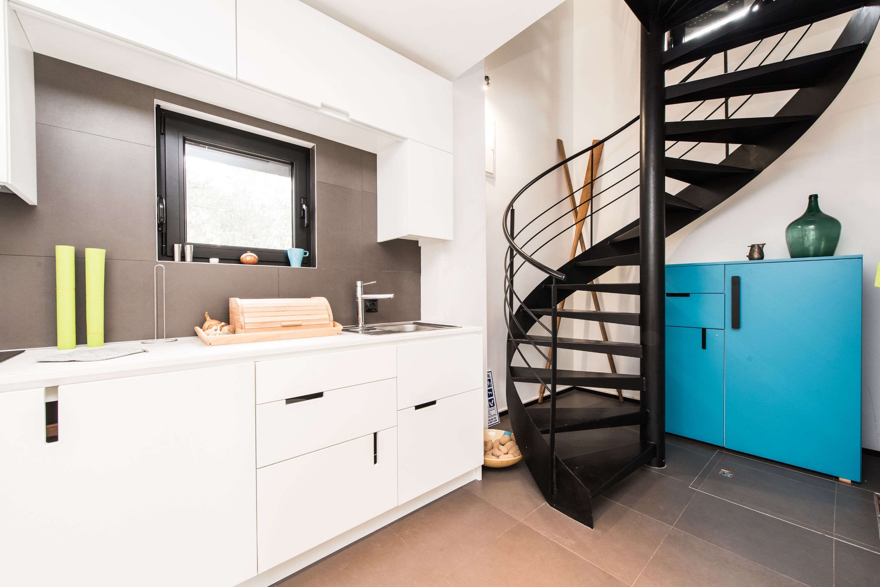 A modern kitchen with white cabinets, a black spiral staircase, and a blue cabinet.