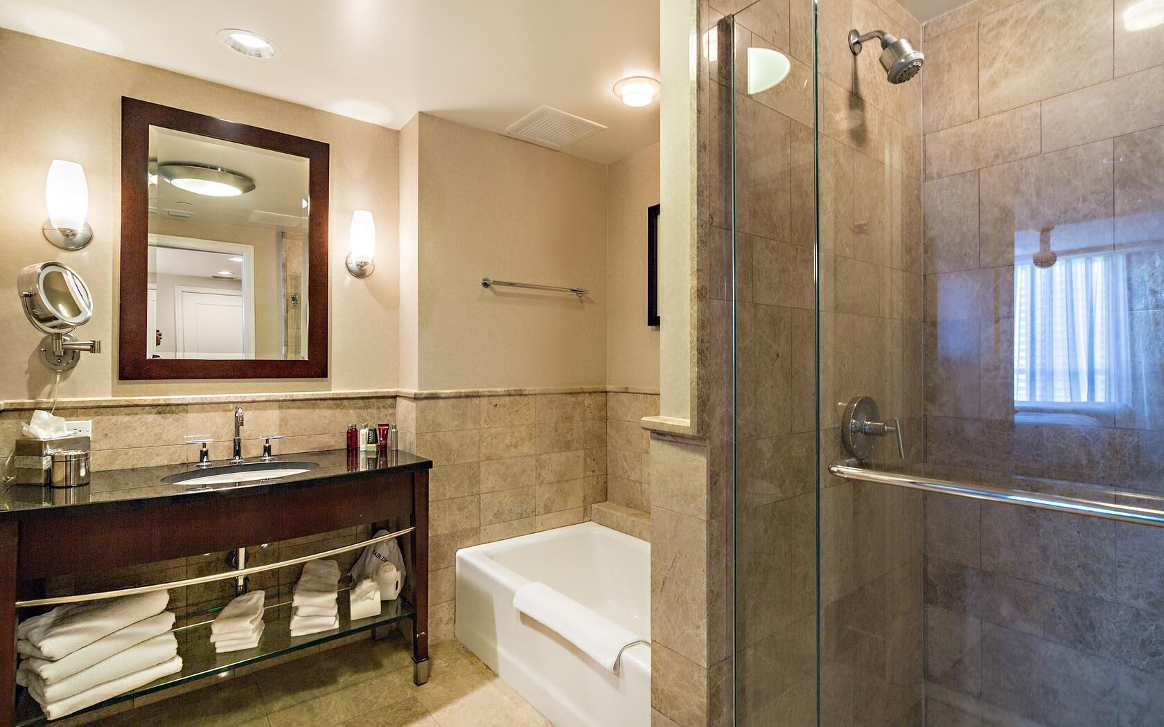 A modern bathroom with a glass-enclosed shower, a standalone bathtub, and a vanity with a mirror and lighting.