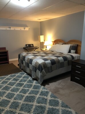 A bedroom with a bed, a nightstand, a lamp, a desk, and a chair.
