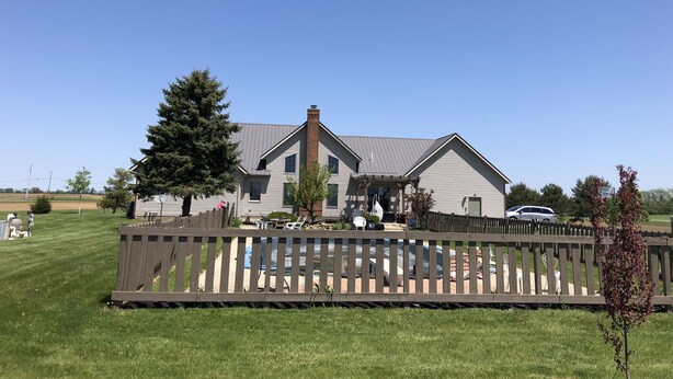 A two-story house with a large front yard, a wooden fence, and a car parked in the driveway.