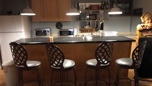 A kitchen with wooden cabinets, a microwave, a sink, and four bar stools.