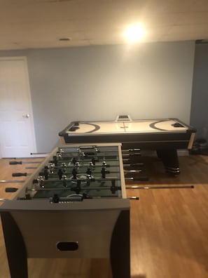 Una habitación con dos mesas de fútbol de mesa, piso de madera y una puerta blanca.