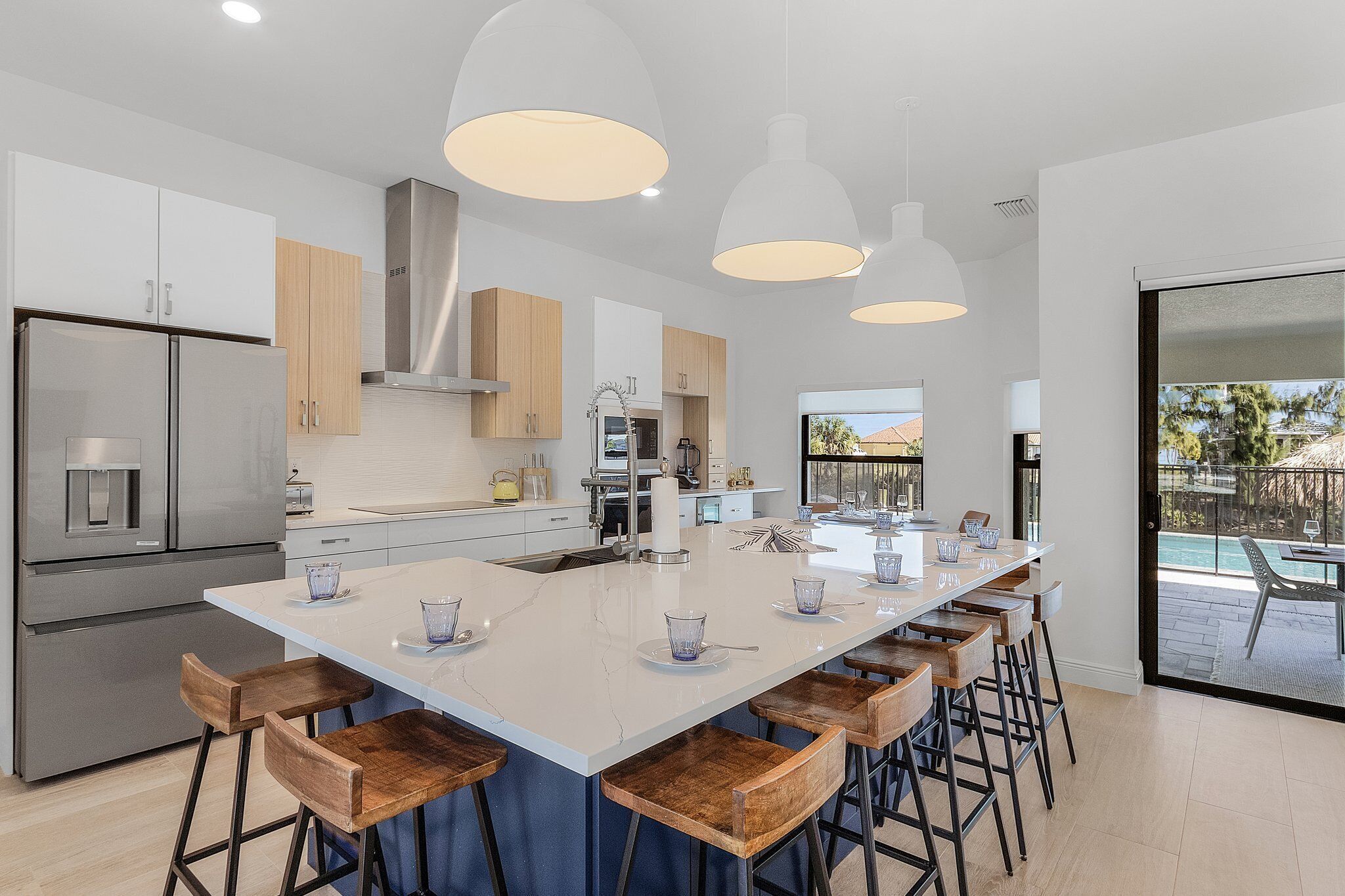 Uma cozinha moderna com uma ilha grande, eletrodomésticos de aço inoxidável, banquetas de madeira e iluminação pendente.