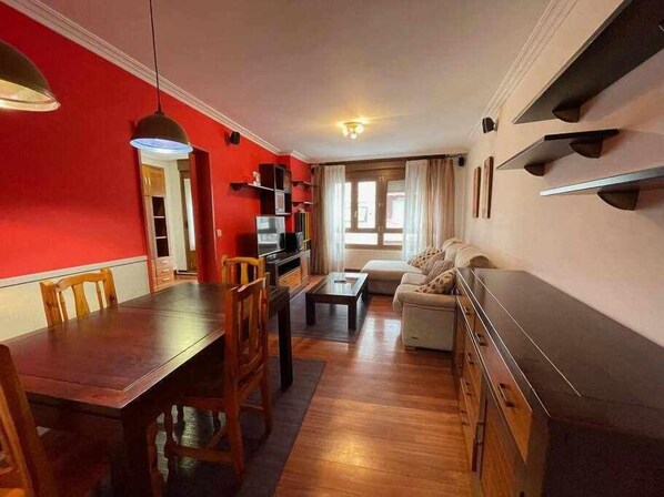 A dining area with a wooden table and chairs, a sofa, and a TV on a shelf.