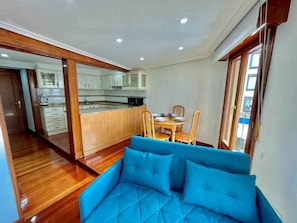 Apartamento moderno com cozinha compacta, sala de jantar e sofá azul.