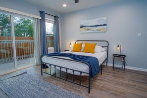 A bedroom with a bed, a nightstand, a lamp, a painting, and a view of the outdoors.