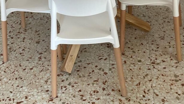 Una mesa redonda blanca con dos sillas blancas, una puerta de madera y una pared blanca.