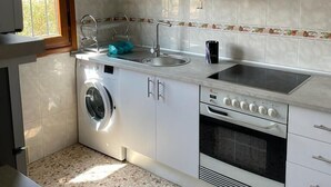 Una cocina compacta con armarios blancos, lavadora integrada, estufa y lavabo.