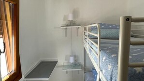 Dormitorio con literas, una ventana, un escritorio y una lámpara colgante.