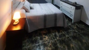 A bedroom with a bed, bedside tables, a dresser, a ceiling fan, and a window with curtains.