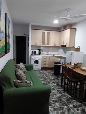 Un espacio habitable compacto con sofá verde, mesa de comedor con sillas, lavadora, microondas y refrigerador.