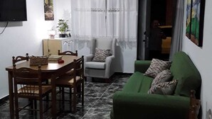 A compact living space with a dining table, chairs, a green sofa, a ceiling fan, and a TV mounted on the wall.