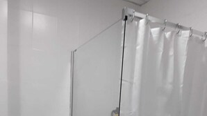 A bathroom with a glass shower enclosure, a toilet, and a marble floor.