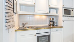 Eine moderne Küche mit weißen Schränken, einer Edelstahl-Spüle, einer Kaffeemaschine und einer Mikrowelle.