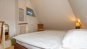 Ein Schlafzimmer mit einem großen Bett, einer Holzleiter, einer weißen Heizung, einem Korbstuhl und einem an der Wand montierten Fernseher.