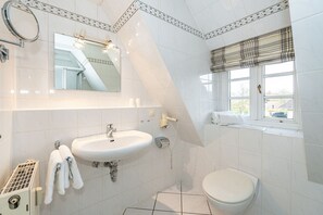 Une salle de bain équipée d’un lavabo, d’un miroir, d’un porte-serviettes, de toilettes et d’une fenêtre donnant sur un paysage agréable.