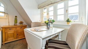 Ein Essbereich mit einem weißen Tisch, einem gestreiften Stuhl, einer Holzkabine und einem Fenster mit Vorhängen.