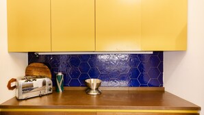 Una cocina con armarios amarillos, un salpicadero de azulejos hexagonales azules, un tostador de acero inoxidable y un bol de metal sobre la encimera.