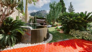 Un jardín con una fuente circular, diversas plantas y vistas a la montaña.