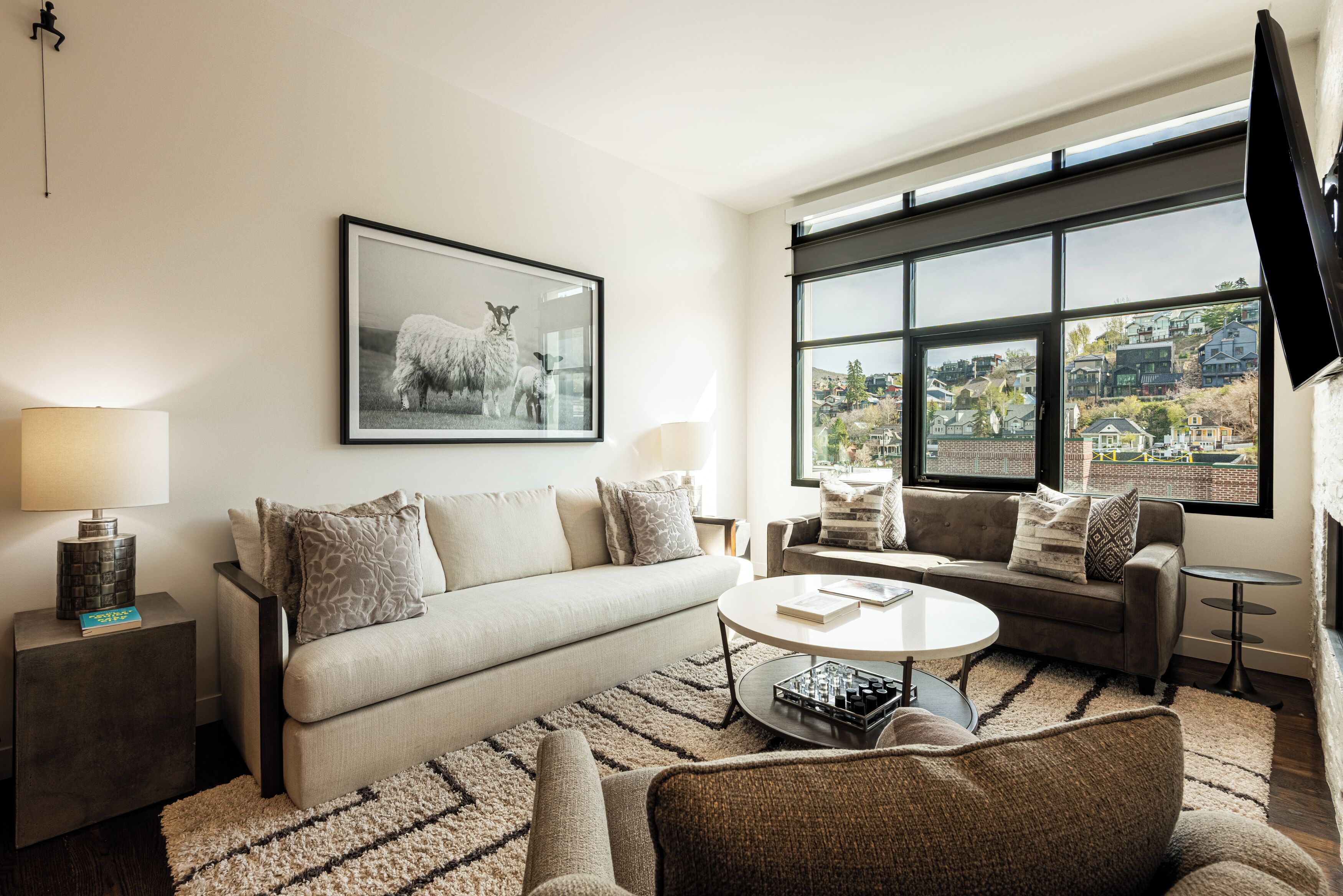 A modern living room with a sofa, a coffee table, and a large window offering a city view.