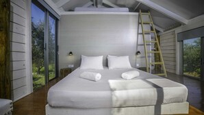 Un grand lit avec du linge de lit blanc, deux lampes de chevet et une échelle en bois.