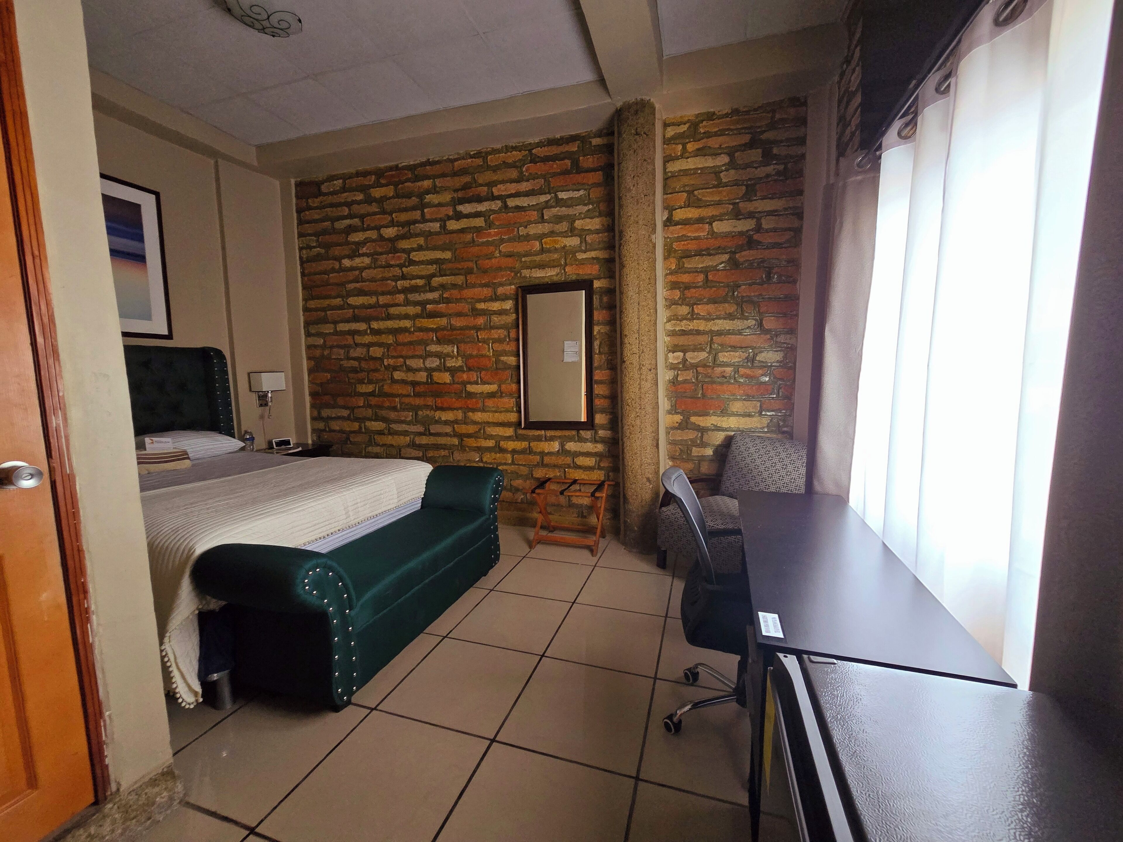Une chambre d’hôtel avec un mur en briques, un lit, un canapé vert, un bureau et une chaise.