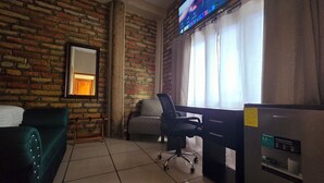 A room with a brick wall, a desk with a chair, a bed, and a TV mounted on the wall. - Hotel el Campanario (Comayagua)