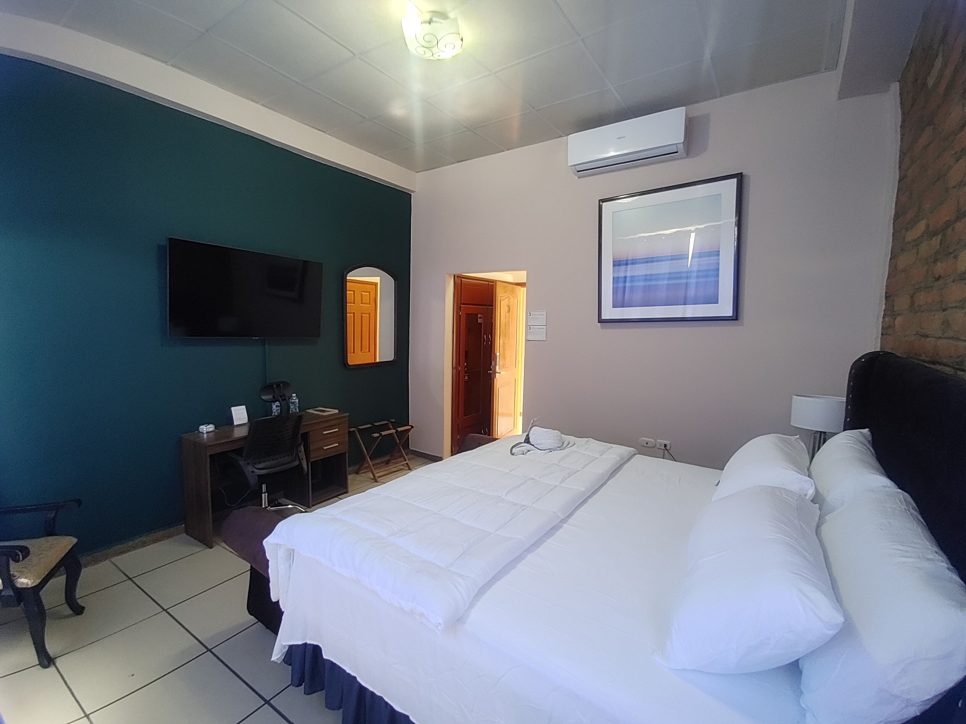 A hotel room with a bed, a desk, a chair, a TV, and an air conditioning unit.