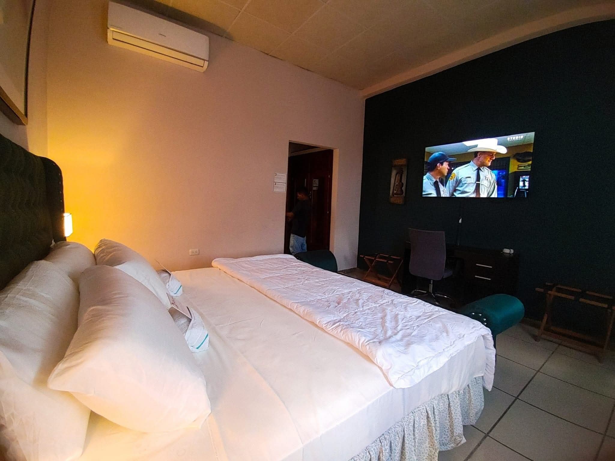A hotel room with a large bed, a television on the wall, and a door leading to another room.
