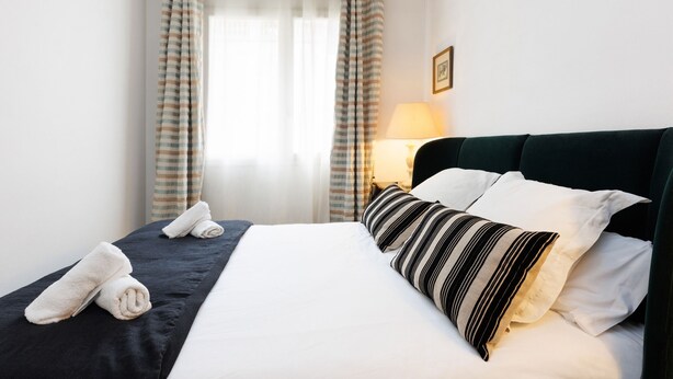A neatly made bed with white and striped pillows, a dark headboard, and a pair of folded towels on the side.