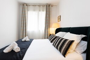 A neatly made bed with white and striped pillows, a dark headboard, and a pair of folded towels on the side. - Apartment 3 bedrooms 4 pax in the city center - FREE WIFI (Barcelona)