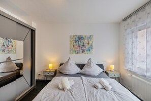 Une chambre d’hôtel avec un lit, deux tables de chevet, un miroir, une fenêtre avec des rideaux à motifs floraux et une œuvre d’art abstraite au mur.