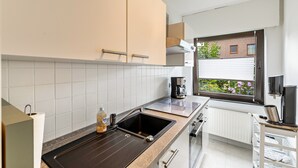Une cuisine moderne équipée d’une cuisinière intégrée, d’une machine à café et d’une fenêtre donnant sur un bâtiment en briques et sur de la verdure.