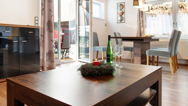 Un coin repas avec une table, des chaises, une bougie et une bouteille.