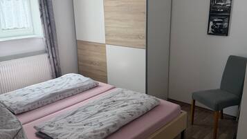 Una camera da letto con un letto, una sedia, una finestra con tende, un lampadario a parete e un quadro incorniciato.
