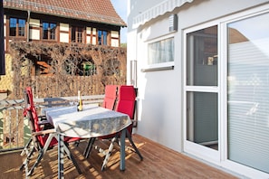 Un patio con una mesa y sillas, una silla roja, una botella y una ventana con persianas.