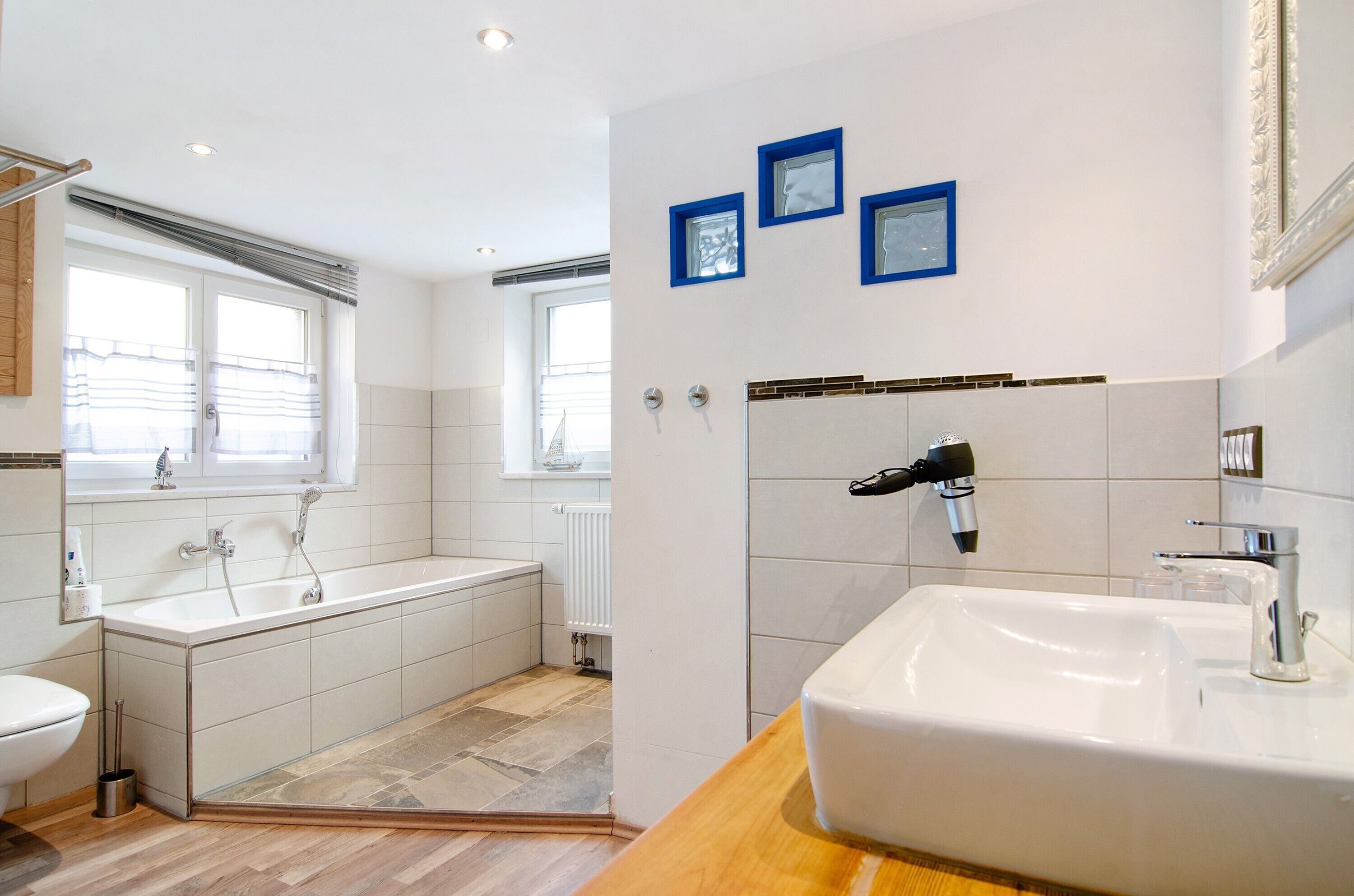 A modern bathroom with a bathtub, a sink, and a toilet. There are three framed pictures on the wall, and a window with a towel rack.