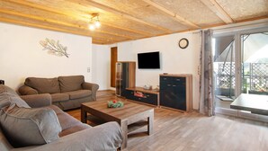 Un salon comprenant un canapé, une table basse, un téléviseur à écran plat et une porte-fenêtre coulissante donnant sur un espace extérieur.