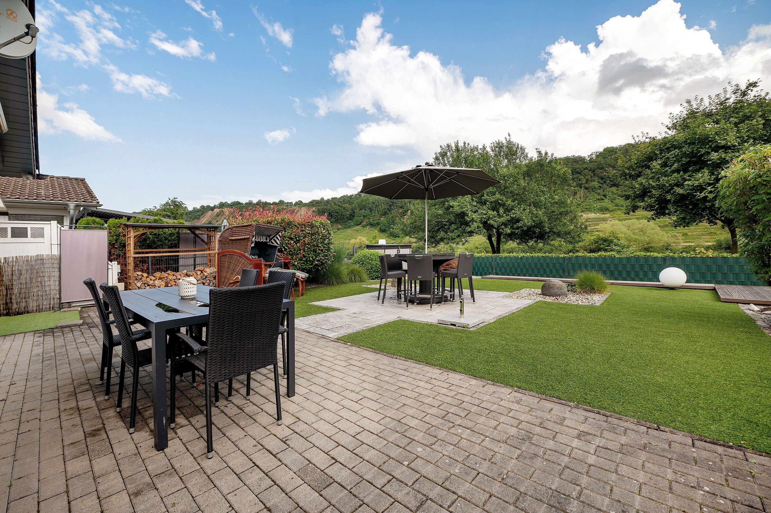 Eine Terrasse mit Tisch, Stühlen, einem Grill und einem großen Sonnenschirm.